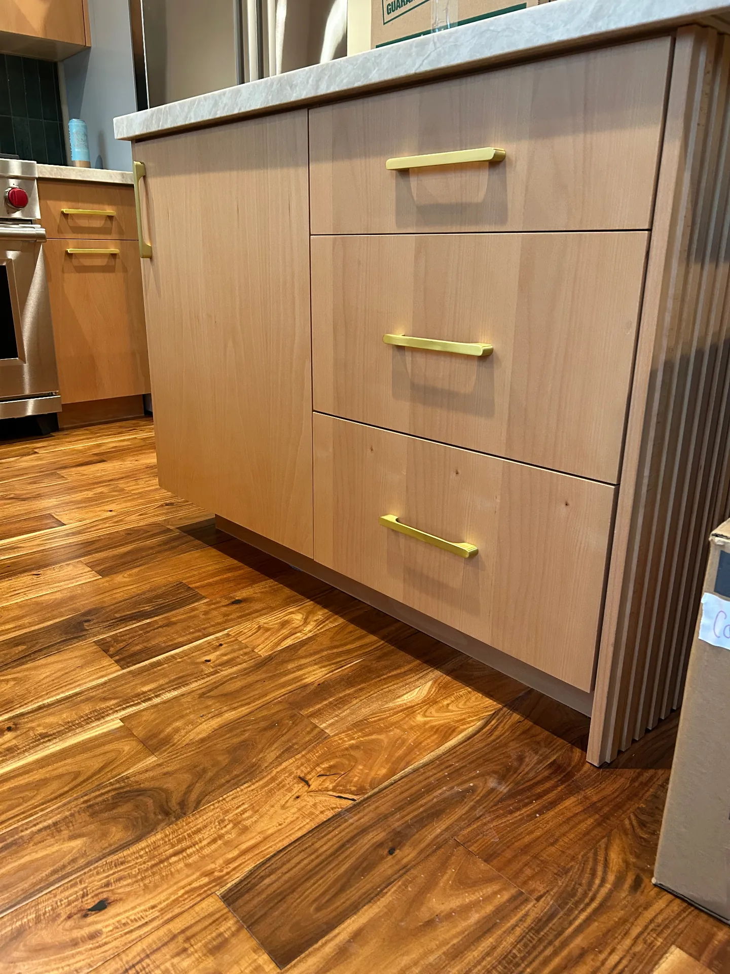Detail of finished stained kitchen island with brass pulls and acacia wood floor