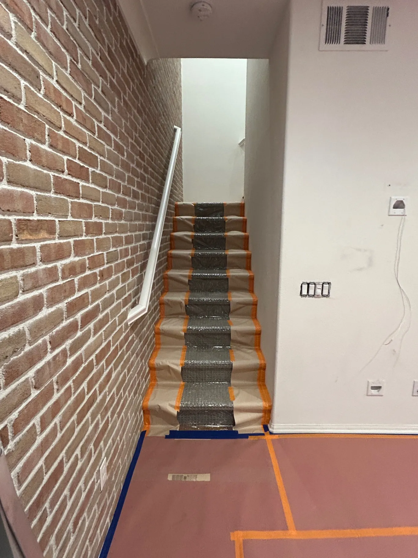 Stairwell with exposed brick accent wall masked and protected for paint