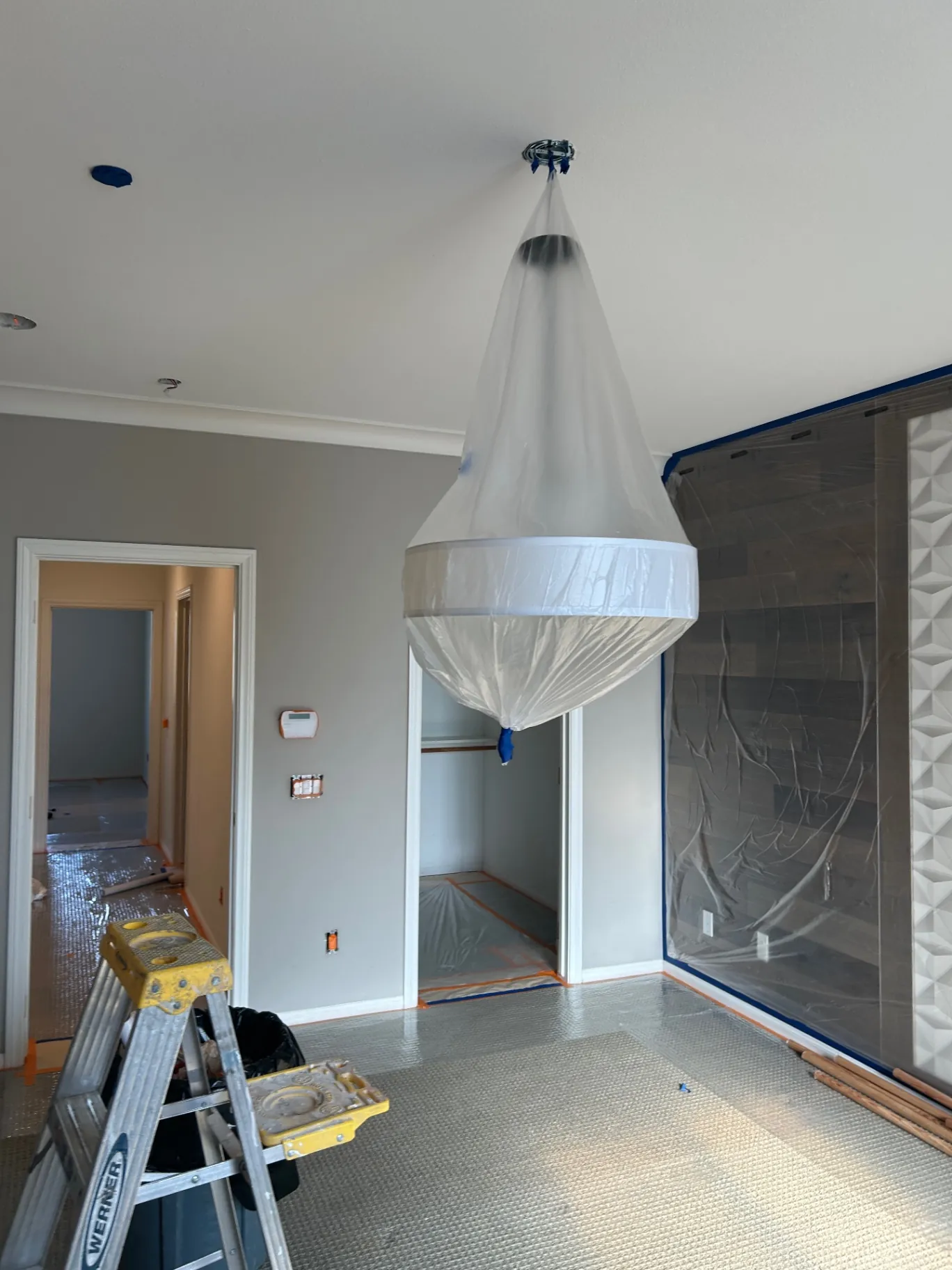 Interior living area with masked chandelier and floor protection during prep